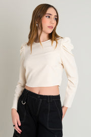 Blusa de cuello redondo, manga larga de hombro abullonado y escote en espalda. Cierre posterior con botón, ojal y lazo amarrable.