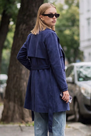 Abrigo trench corto de gamuza, fit recto, cuello solapa, bolsillos delanteros con vivos, detalle de bata frontal y posterior, manga larga con trabillas en puños, cinturón amarrable del mismo tejido y cierre frontal con doble cruce de botones en contraste.