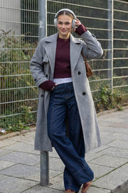 Abrigo largo de doble cruce de botón en contraste, manga larga con trabilla y botón en puños, con solapa, bata decorativa frontal, bolsillos delanteros con vivos, trabillas y cinturón amarrable del mismo tejido.