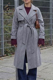 Abrigo largo de doble cruce de botón en contraste, manga larga con trabilla y botón en puños, con solapa, bata decorativa frontal, bolsillos delanteros con vivos, trabillas y cinturón amarrable del mismo tejido.