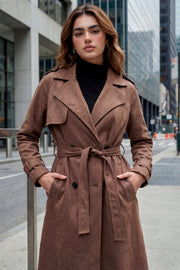 Abrigo trench midi de gamuza, fit recto, con solapa, bolsillos delanteros con vivos, detalle de bata frontal, manga larga con trabillas en puños y hombros, cinturón amarrable del mismo tejido y cierre frontal con doble cruce de botones en contraste.