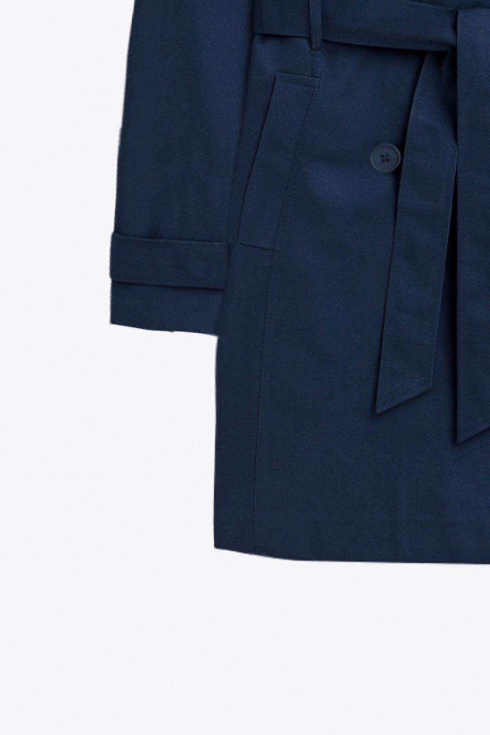 Abrigo trench corto de fit recto, con cuello solapa, bolsillos delanteros con vivos, detalle de bata trasera y manga larga. Trabillas, cinturón amarrable del mismo tejido y cierre frontal con doble cruce de botones en contraste. Detalle de trabilla y botón en hombros, bata trasera, cuello y puños.