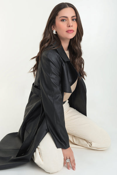 Abrigo trench largo de efecto piel, fit recto, manga larga, con solapa y bata en espalda, cortes decorativos frontales, trabillas y cinturón del mismo tejido con hebilla en contraste. Cierre frontal con doble cruce de botones en contraste.