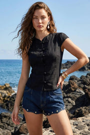 Blusa corta de fit ajustado, cuello mao, manga corta con plisados en hombros, cierre frontal con botones y detalle de lazo amarrable posterior.