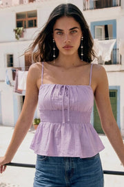 Blusa corta de tirantes delgados ajustables, escote redondeado con plisados y lazo frontal decorativo, fruncido en cintura y peplum de olanes en bajo.