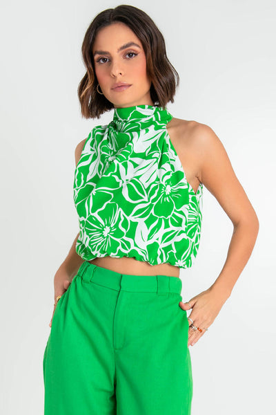 Blusa asimétrica corta de estampado floral, sin mangas, de cuello alto con plisados en hombros, fit abullonado con rib elástico en bajo y cierre posterior con botón y ojal.  