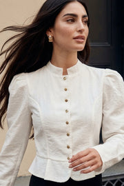 Blusa de fit ajustado, manga larga con hombros abullonados, cuello mao, pinzas frontales, peplum con olanes en bajo y cierre frontal con hilera de botones en contraste.
