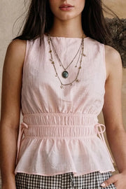Blusa corta de cuello barco, sin mangas, rib con plisados en cintura, peplum con olanes en bajo y detalle de jaretas ajustables en costados. Cierre posterior con botón y ojal.