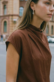 Blusa de cuello alto fluido, plisados en hombros, manga corta seguida y fit recto. Cierre posterior con botón y ojal.