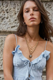 Blusa corta de tirantes delgados ajustables, escote v con olanes en borde, cortes frontales con plisados, peplum con olanes en bajo y cierre frontal con lazos amarrables.