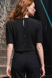 Blusa corta de fit recto, cuello redondo, manga corta abullonada y cierre posterior con hilera de botones en contraste.
