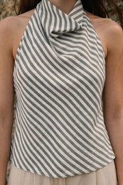 Blusa corta de estampado rayas, fit fluido, sin mangas, cuello halter fluido con plisados, escote en espalda y lazo amarrable posterior. Cierre posterior con botón y ojal.