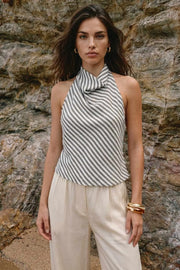 Blusa corta de estampado rayas, fit fluido, sin mangas, cuello halter fluido con plisados, escote en espalda y lazo amarrable posterior. Cierre posterior con botón y ojal.