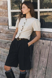 Blusa corta de fit ajustado, cuello redondo, manga corta con plisados en hombros, cortes frontales, bajo curveado frontal y cierre con hilera de botones en contraste.