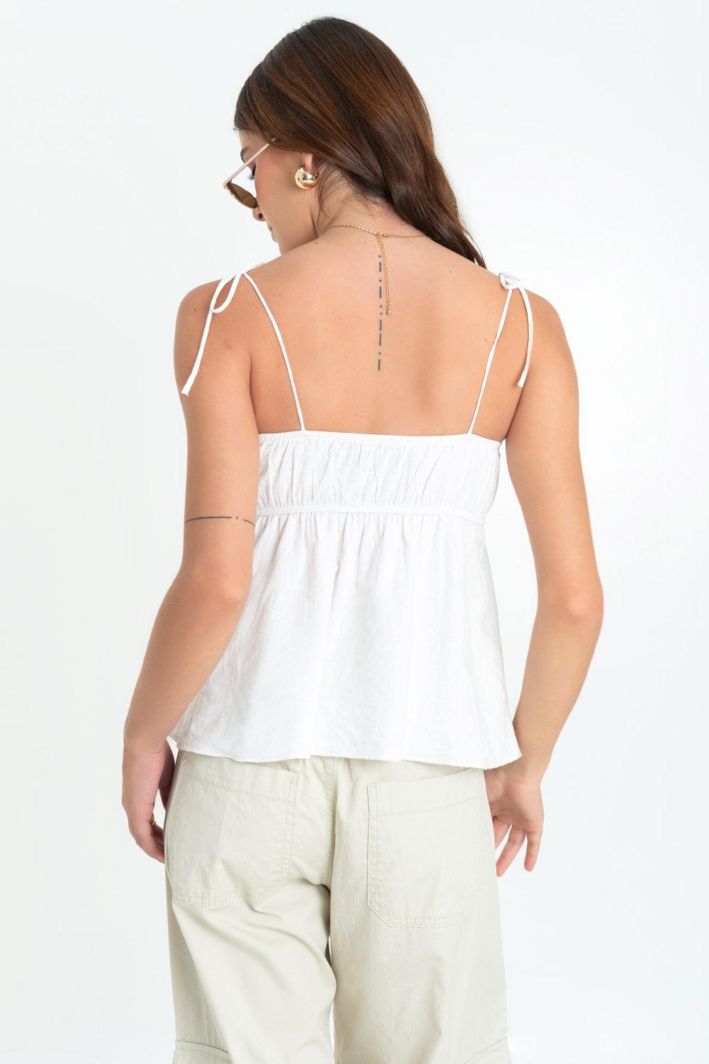 Blusa corta de fit fluido, tirantes delgados con nudo amarrable, escote v redondeado con cortes decorativos, plisados y olanes en bordes. Detalle de rib elástico posterior.