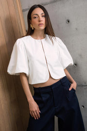 Blusa corta de fit recto, cuello redondo, manga corta amplia globo con volumen en borde, cierre frontal con broches ocultos y bajo curveado frontal.