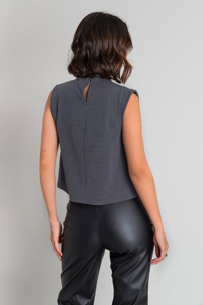 Blusa corta de fit recto, sin mangas, cuello alto seguido con plisados, cierre posterior con botón y ojal.