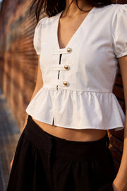 Blusa corta de fit recto, manga corta abullonada con rib elástico en bordes, escote v, peplum con olanes y cierre frontal con hilera de botones en contraste.