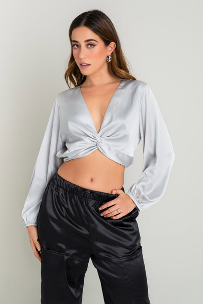 Blusa corta satinada con hombreras, escote v con nudo, fit ajustado y manga larga abullonada con rib elástico en puños. Detalle de rib elástico posterior en cintura.