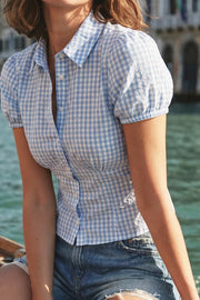 Camisa corta de estampado cuadros, fit recto, manga corta abullonada con rib elástico en bordes, cuello camisero, cortes y plisados frontales. Cierre frontal con hilera de botones.