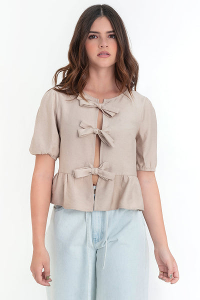 Blusa de manga corta abullonada con rib elástico en bordes, cuello redondo y cierre frontal con lazos amarrables. Detalle de peplum con olanes en bajo.