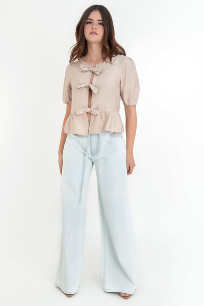 Blusa de manga corta abullonada con rib elástico en bordes, cuello redondo y cierre frontal con lazos amarrables. Detalle de peplum con olanes en bajo.