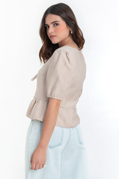 Blusa de manga corta abullonada con rib elástico en bordes, cuello redondo y cierre frontal con lazos amarrables. Detalle de peplum con olanes en bajo.