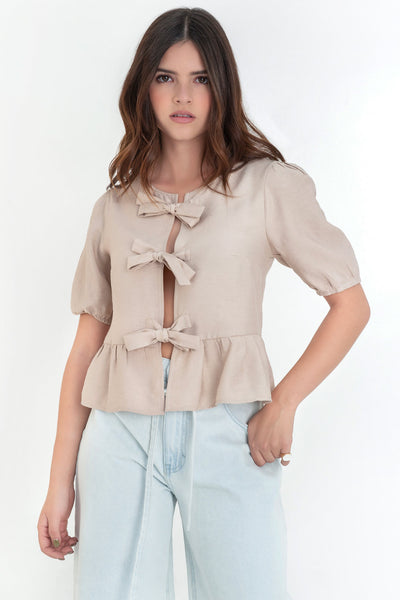 Blusa de manga corta abullonada con rib elástico en bordes, cuello redondo y cierre frontal con lazos amarrables. Detalle de peplum con olanes en bajo.