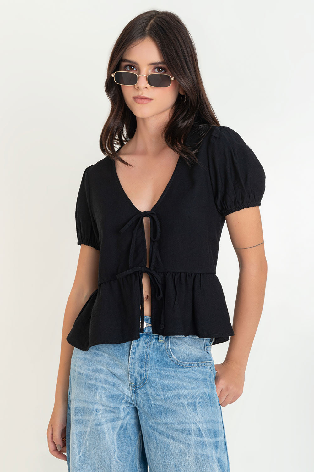 Blusa de manga corta abullonada con rib elástico en bordes, escote v y cierre frontal con lazos amarrables. Detalle de peplum con olanes en bajo.