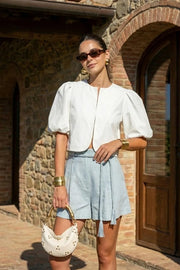 Blusa corta de fit recto, cuello redondo, manga corta amplia globo con volumen en borde, cierre frontal con broches ocultos y bajo curveado frontal.