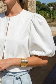 Blusa corta de fit recto, cuello redondo, manga corta amplia globo con volumen en borde, cierre frontal con broches ocultos y bajo curveado frontal.