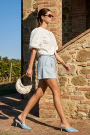 Blusa corta de fit recto, cuello redondo, manga corta amplia globo con volumen en borde, cierre frontal con broches ocultos y bajo curveado frontal.