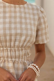 Blusa de estampado cuadros, manga corta abullonada con plisados en hombros, cuello redondo, rib elástico en cintura y peplum con olanes en bajo. Cierre posterior con botón y ojal.
