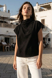 Blusa fluida de manga corta seguida, cuello mock seguido con plisados decorativos en hombro y cuello. Cierre posterior con botones y ojales.