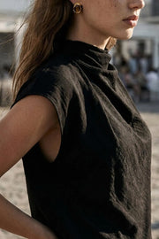 Blusa fluida de manga corta seguida, cuello mock seguido con plisados decorativos en hombro y cuello. Cierre posterior con botones y ojales.