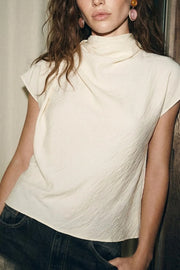 Blusa fluida de manga corta seguida, cuello mock seguido con plisados decorativos en hombro y cuello. Cierre posterior con botones y ojales.