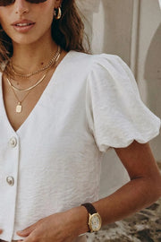 Blusa corta de fit recto, escote v, manga corta abullonada y cierre frontal con hilera de botones en contraste.