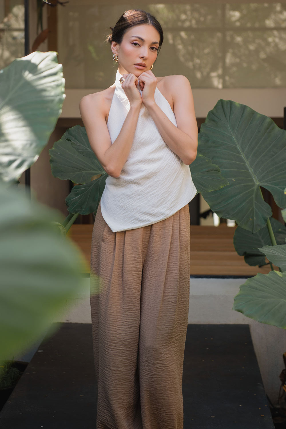 Blusa fluida de cuello alto halter con plisados, sin mangas, escote en espalda y bajo frontal asimétrico. Cierre posterior con broches.