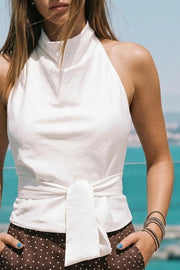 Blusa de fit recto, halter con cuello fluido, sin mangas, lazo amarrable en cintura, cierre posterior con botón y ojal.