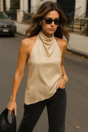 Blusa halter de cuello alto fluido, sin mangas, fit recto, escote en espalda y bajo asimétrico frontal. Cierre posterior con botón y ojal.