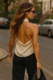 Blusa halter de cuello alto fluido, sin mangas, fit recto, escote en espalda y bajo asimétrico frontal. Cierre posterior con botón y ojal.