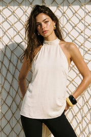 Blusa larga de fit fluido, cuello alto halter, sin mangas, escote en espalda con lazo amarrable posterior y detalle posterior con bajo asimétrico.