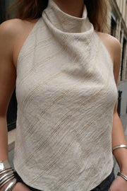 Blusa corta de fit fluido, sin mangas, estampado rayas, cuello halter fluido con plisados, escote en espalda y lazo amarrable posterior. Cierre posterior con botón y ojal.