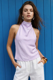 Blusa corta de fit fluido, sin mangas, cuello halter fluido con plisados, escote en espalda y lazo amarrable posterior. Cierre posterior con botón y ojal.