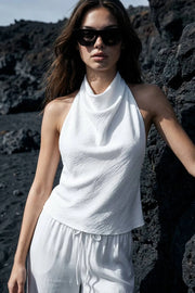 Blusa corta de fit fluido, sin mangas, cuello halter fluido con plisados, escote en espalda y lazo amarrable posterior. Cierre posterior con botón y ojal.