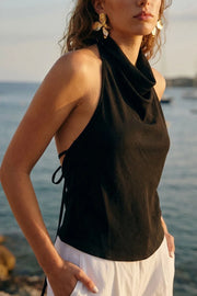 Blusa corta de fit fluido, sin mangas, cuello halter fluido con plisados, escote en espalda y lazo amarrable posterior. Cierre posterior con botón y ojal.