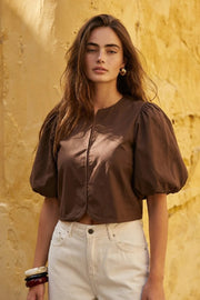 Blusa corta de fit recto, cuello redondo, manga corta amplia globo con volumen en borde, cierre frontal con broches ocultos y bajo curveado frontal.
