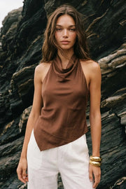 Blusa asimétrica de fit fluido, sin mangas, cuello halter fluido con plisados, escote en espalda y lazo amarrable posterior. Cierre posterior con botón y ojal. Detalle de bajo frontal asimétrico.