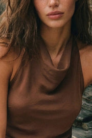 Blusa asimétrica de fit fluido, sin mangas, cuello halter fluido con plisados, escote en espalda y lazo amarrable posterior. Cierre posterior con botón y ojal. Detalle de bajo frontal asimétrico.