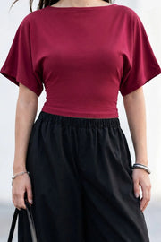 Blusa corta de fit ajustado, cuello barco, manga corta seguida con olanes y nudo amarrable posterior.